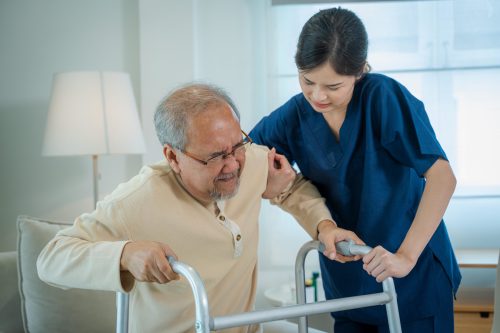 Caregiver assisting senior man to walk with walker during recovery at nursing home.